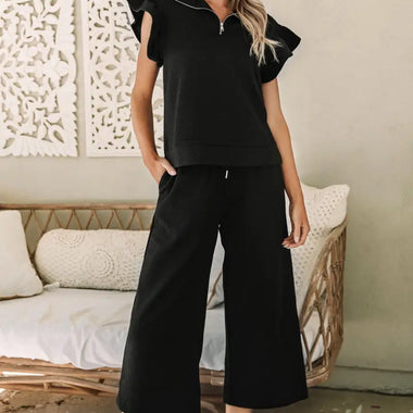 Woman wearing a black textured flutter sleeve top and wide-leg pants, sizes bust waist available