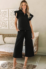 Woman wearing a black textured flutter sleeve top and wide-leg pants, sizes bust waist available