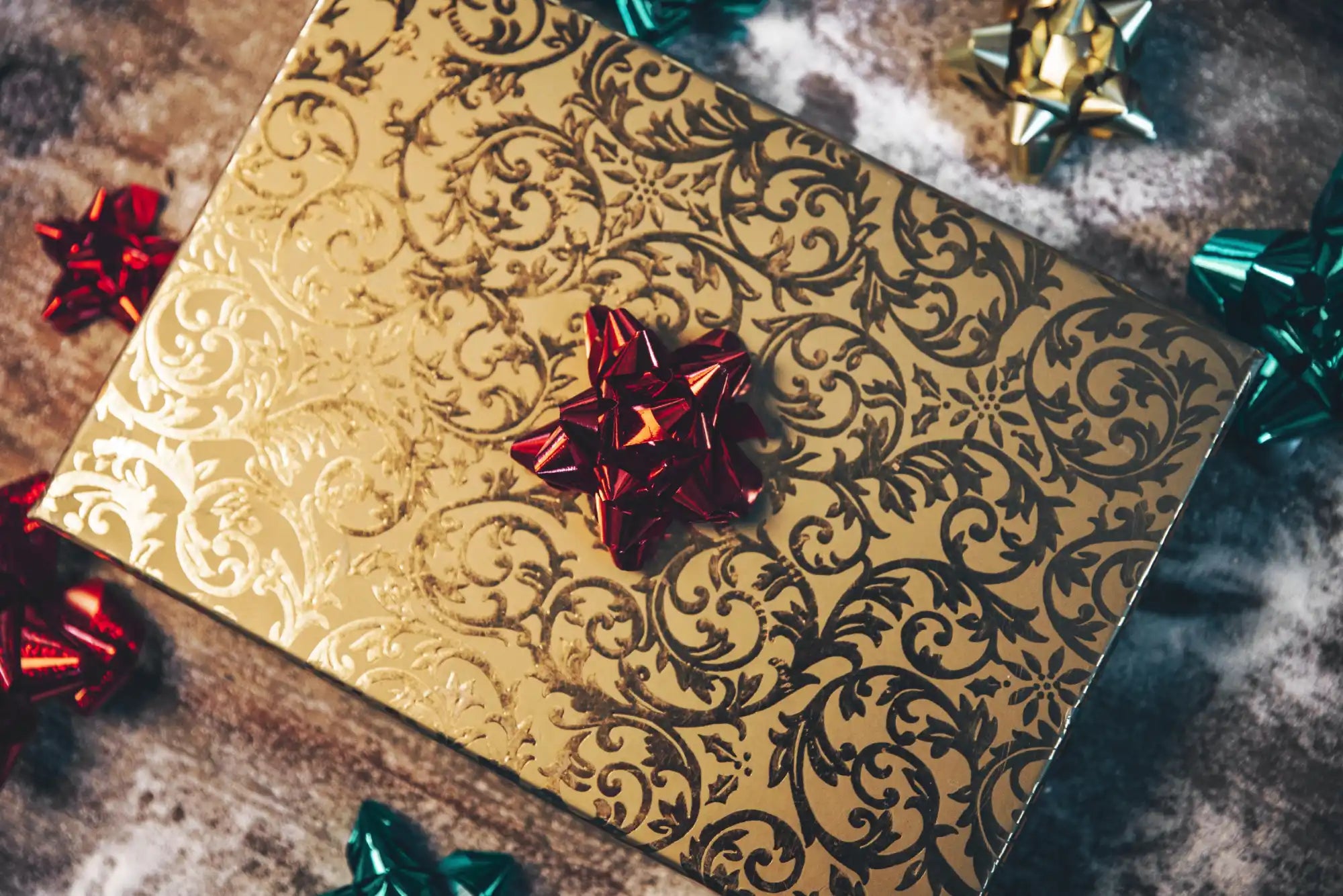 Gold-patterned gift box with an ornate swirling design and a red bow on top.