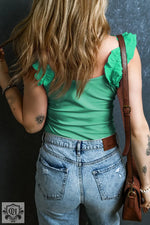 Woman wearing a mint green ruffled tank top with wide straps and jeans